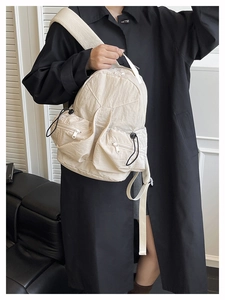 Detail view of the multi-pocket cream nylon functional backpack on model in black coat