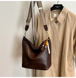 Detail of soft brown leather bucket bag with bohemian beaded charms and patterned strap