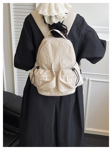 Detail of beige nylon backpack showing dual zippered pockets and black drawstrings
