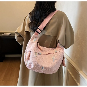 Detailed shot of pink half-moon bag with colorful butterfly embroidery on beige coat