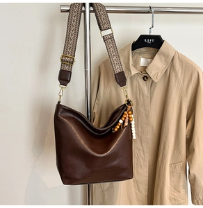 Detail of dark brown leather bucket bag with colorful woven strap and beaded charm