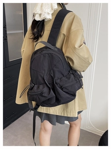 Detail view of a black lightweight nylon backpack featuring side drawstring pockets and zippers