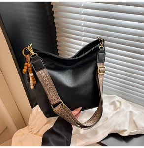 Detail of black hobo bag showing woven jacquard strap and wooden bead pendant accessory