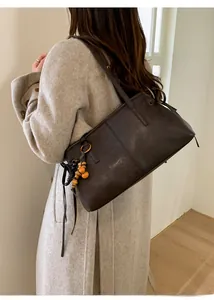 Detail of dark brown leather tote bag featuring drawstring bow and wooden bead charm