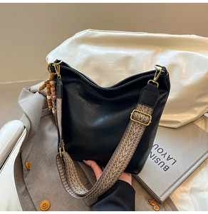 Detail of soft black leather tote with ethnic woven strap and wooden bead charm accent