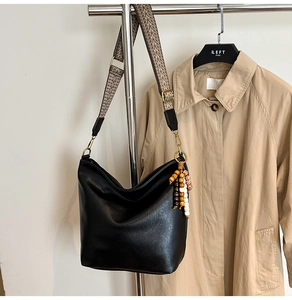 Detail of black faux leather bucket bag featuring a colorful woven strap and wood bead tassel
