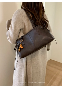 Detail of dark brown leather tote featuring colorful wooden bead charm and long side straps