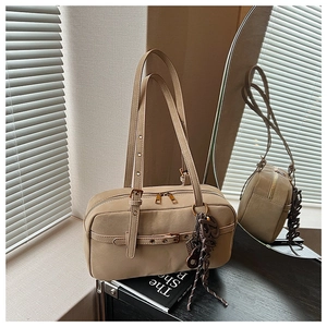 Detailed close-up of beige underarm bag with zipper, buckle, and letter charm detail