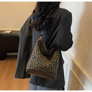 Detail of leopard print bucket bag with leather trim on model in indoor setting