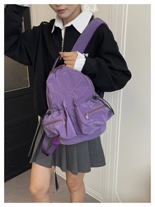 Detail of purple nylon backpack with crinkled texture and side zipper pocket on a model