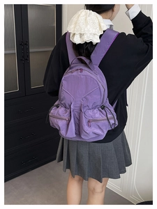 Detail view of purple nylon backpack showing front zipper pockets and pleated texture