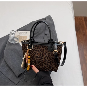 Dettaglio della borsa leopardata con manici in pelle nera e ciondolo nappa in legno