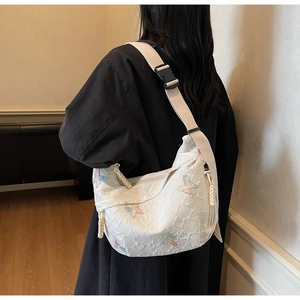Detail of white quilted crossbody bag featuring colorful butterfly embroidery and wide strap