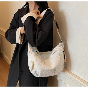 Detail of white quilted crescent bag with butterfly embroidery and woven cord accents
