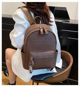Detail of dark brown woven leather backpack with a silver bear charm in office setting