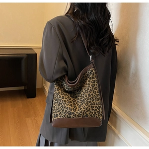 Detailed side view of leopard print bucket bag with dark brown leather straps on model