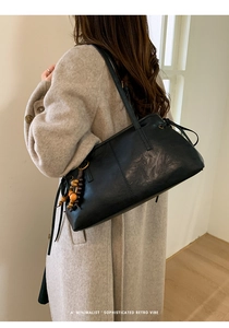 Detail of black leather shoulder bag with vintage wooden bead charm and minimalist retro design