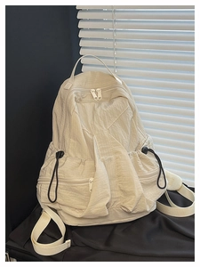 Detail view of the beige nylon backpack showing drawstring side pockets and fabric texture
