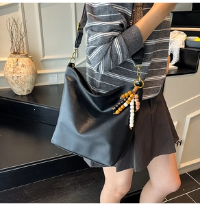 Detail of black leather hobo bag featuring bohemian woven strap and wood bead accessory