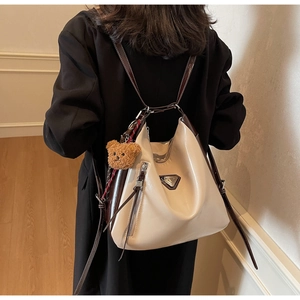 Detail view of stylish beige and brown tote backpack featuring a plush bear charm and metal logo