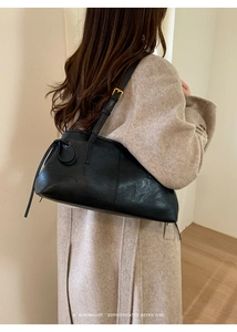 Detail of minimalist black leather shoulder bag styled with a beige wool coat