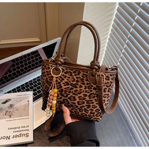 Borsa a secchiello leopardata con nappina in legno vicino a laptop e libri di design