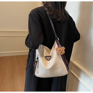 Detail of cream white faux leather bucket bag with brown straps and cute plush bear charm