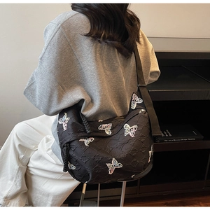 Detail of black quilted canvas bag featuring colorful butterfly embroidery and wide strap