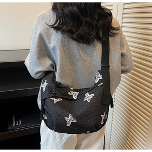 Detail of black quilted crossbody bag featuring colorful butterfly embroidery and wide strap