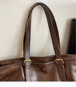 Detail of adjustable flat shoulder strap with gold buckle on a brown leather tote bag