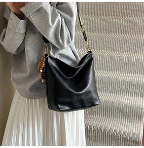 Detail of black soft leather bucket bag with wood bead charm and patterned wide strap