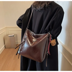 Detail of glossy brown faux leather shoulder bag with silver triangle decor and bear charm