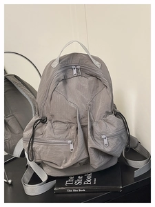 Detail view of the gray lightweight nylon backpack showing multiple zipper pockets and texture