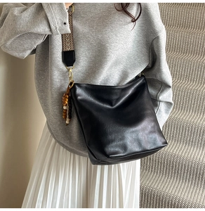 Detail of black soft leather bucket bag with bohemian woven shoulder strap and wood beads