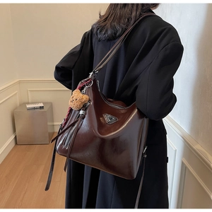 Detail of dark brown leather bucket bag with teddy bear pendant and striped scarf accessory
