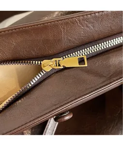 Detail of dark brown leather tote featuring a smooth golden metal zipper puller