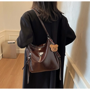 Detail of a brown patent leather hobo bag with metal triangle decor and plush bear charm