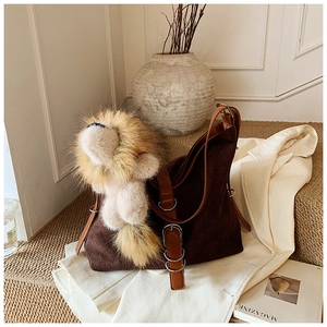 Detail of dark brown suede bucket bag featuring a plush lion charm and leather strap