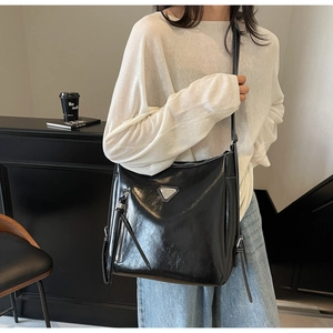 Detail of black leather bucket bag with silver metal triangle logo and decorative side tassels
