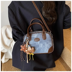 Detail of blue denim pillow bag with brown leather trim and cute bear charm