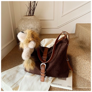 Detail of dark brown tote bag with woven texture, leather straps and fluffy lion charm