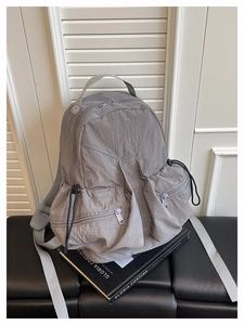 Detail view of grey wrinkled nylon backpack with multiple zipper pockets on a bench