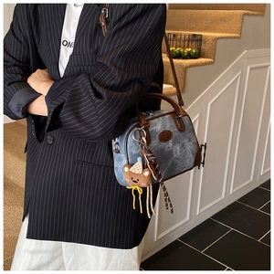 Detail of a blue denim Boston bag with leather trim and cute bear charm on a model