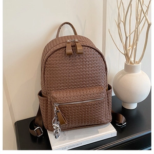 Detail of a brown woven leather backpack with silver bear charm and multi-pocket design