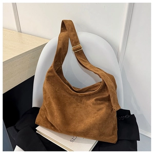 Sac cabas en daim marron avec boucle dorée réglable posé sur une chaise blanche