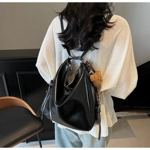 Model wearing a large black shiny leather tote with a cute brown plush bear charm