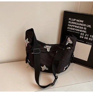 Close-up of black quilted bag featuring colorful butterfly embroidery and wide strap
