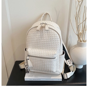 Close-up of woven cream PU leather backpack with silver bear charm on a black desk
