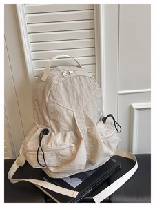 Detail of beige nylon backpack showing drawstring side pockets and metallic zipper puller