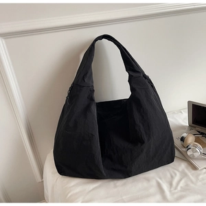 Gros plan d'un grand sac hobo en nylon noir minimaliste avec un ordinateur et un casque